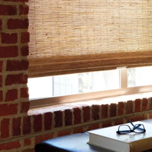 Woven shades on window against brick wall.