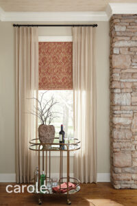 Blush-toned drapery against patterned, red Roman shades.