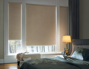 Beige roller shades in the window of a bedroom.